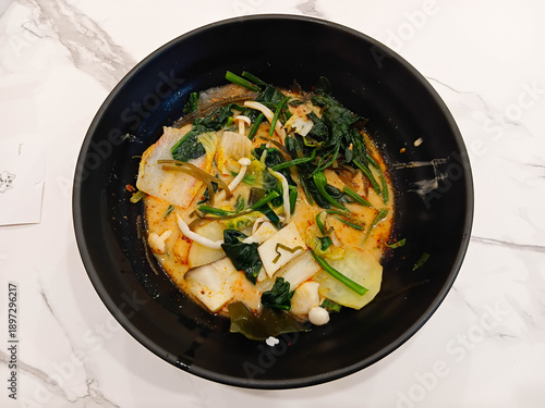 Spicy mala soup served in a black bowl, filled with vegetables and herbs, rich chili broth, hot flavor, Asian comfort food style.
