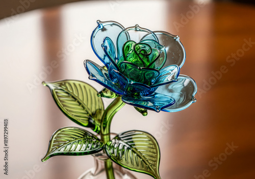 Blue and green glass rose sculpture with leaves on wooden background