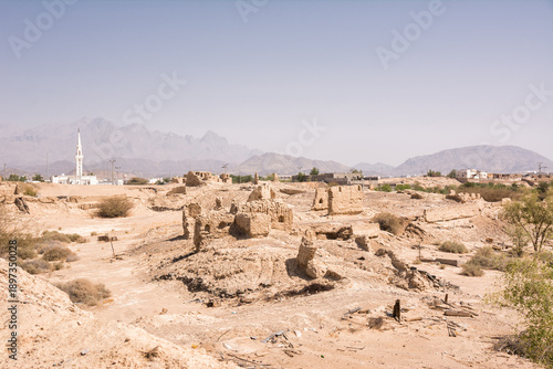 Ruins of an ancient abandoned city with a white mosque minaret in the background in Saudi Arabia