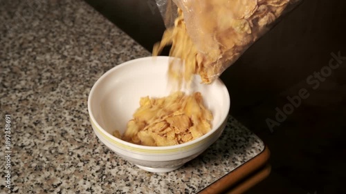 Person pouring cornflake cereal into a white bowl