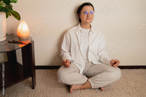 Caucasian female adult practicing meditation at home with incense and salt lamp