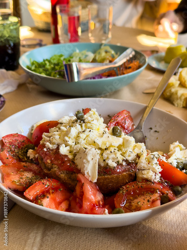 Greek dakos salad with tomatoes, feta cheese, capers and olive oil on barley rusks, served on a table, closeup. Greece
