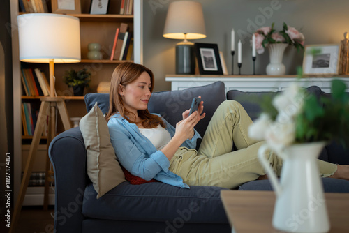 Woman relaxing on sofa, using mobile phone at home