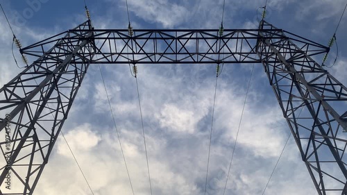 Static upward view of high-voltage gantry as clouds drift slowly across the sky