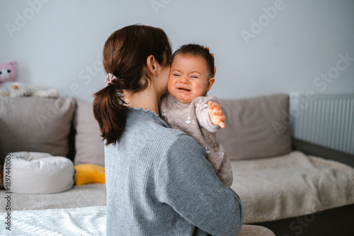 A woman is holding a baby and kissing it. The baby is crying. Scene is sad and tender