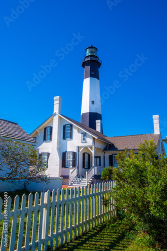 Tybee Island Lighthouse and historic keeper’s cottage behind a white picket fence on a bright sunny day in Georgia.