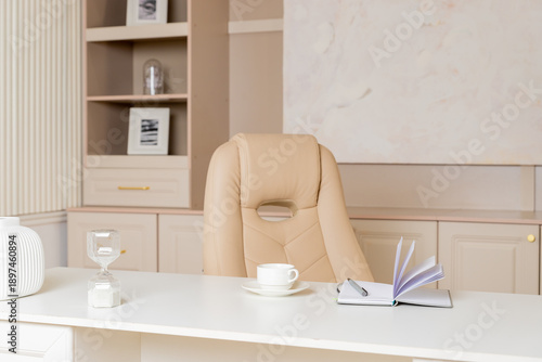 Elegant office desk table. Feminine workspace with paper notebook, cup of coffee, plant, chair. Luxury office interior in pastel colors.
