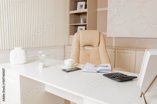 Elegant office desk table. Feminine workspace with paper notebook, cup of coffee, plant, chair. Luxury office interior in pastel colors.