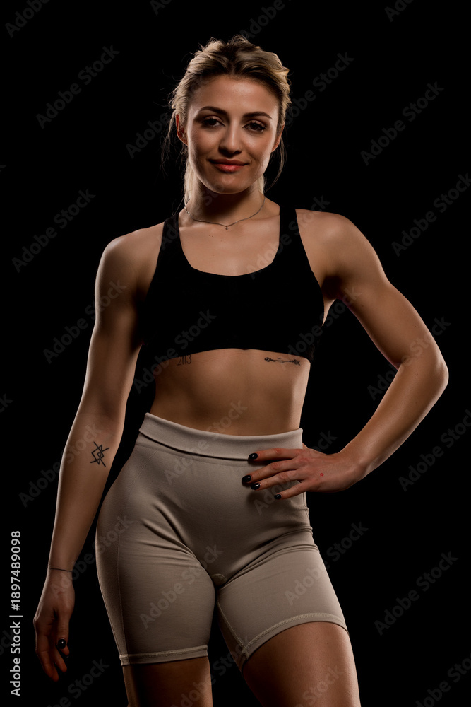 Obraz premium Confident woman in sporty attire posing against a dark background, showcasing fitness and strength in a low-light setting