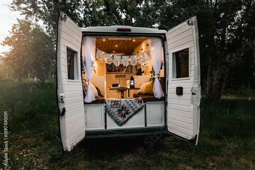 	
Nordic style camper van with decorative lights and boho style hammock in the middle of nature at sunset	
