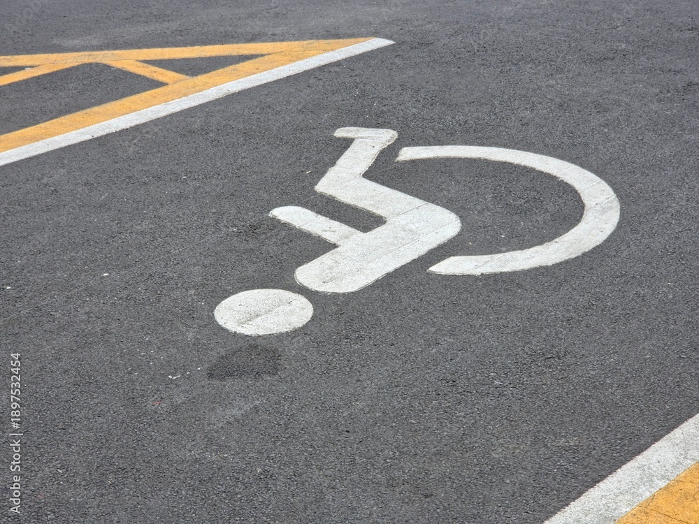 Fototapeta premium High-angle outdoor view of an accessible parking space on dark asphalt, marked with a white wheelchair symbol and bordered by yellow and white directional lines