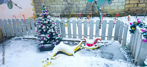 A Christmas tree in the yard on a snowy day. The Christmas deer is covered in snow.