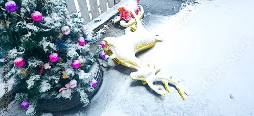 A Christmas tree in the yard on a snowy day. The Christmas deer is covered in snow.