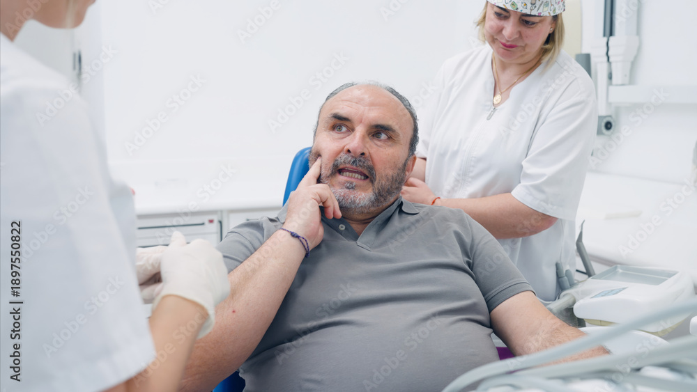 Obraz premium Mature man touching his jaw, experiencing pain or discomfort in his mouth during a dental examination