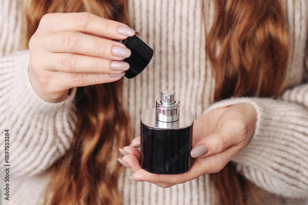 Fototapeta premium Woman holding perfume bottle in hands. Removing cap from fragrance container. Closeup of cosmetic product use. Female hands with beauty product. Daily personal care routine and luxury scent concept.