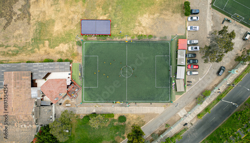 Green soccer field in use by players, top-down drone view.