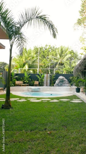Serene backyard of a luxury villa with a swimming pool, green lawn, and lush tropical plants. Idyllic resort for a relaxing vacation. Vertical