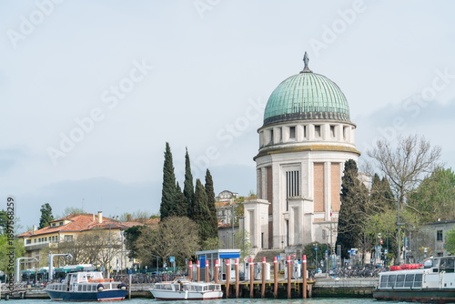 Waterfront view with boats and pier facing the Tempie Votivo di Santa Maria Immacolata with green dome on Lido di Venezia near Venice Italy