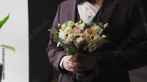 Young handsome groom holding a wedding bouquet in his hand