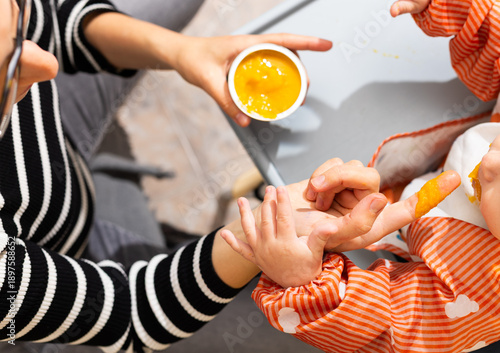 Obraz na płótnie Mother feeding baby puree, making mess with hands