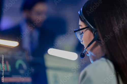 Professional female customer service agent wearing headset working in a modern call center office. Dedicated female consultant providing 24/7 technical support and telemarketing services.