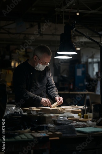 Craftsman Works on Wood Pieces in Workshop With a Lamp in Background at Night
