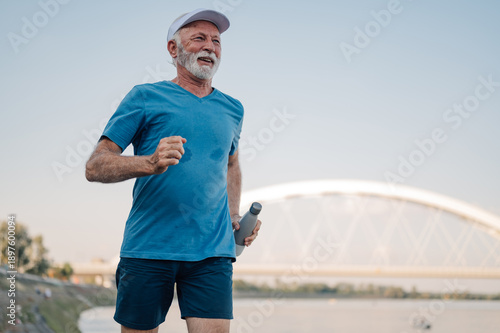 Wallpaper Mural Senior man running near river while holding water bottle Torontodigital.ca