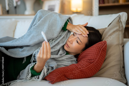 Tableau sur toile Woman experiencing fever checking temperature with thermometer