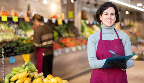 Φωτογραφία Adult woman seller in apron conducting inventory with checklist in vegetable sho