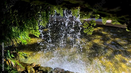 Natural waterfall flowing over rocks in a forest stream. Clear moving water splashes and cascades through stone landscape, creating a fresh summer nature scene.