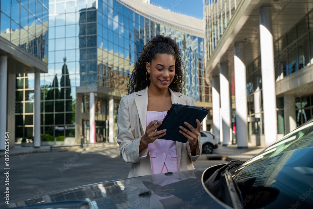 Fototapeta premium Smiling businesswoman interacting with digital tablet in front of modern office buildings