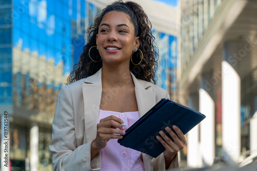 Young woman looking ahead, holding a tablet and stylus in a city environment