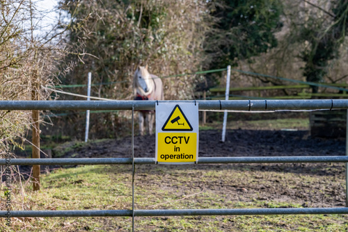Close up of a CCTV sign on the metal gate securing horses in a livery yard