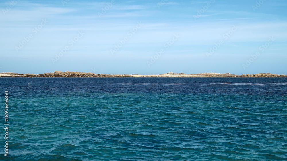 Obraz premium Distant coastline and calm sea beneath a blue sky on the horizon, creating a peaceful and open coastal landscape.