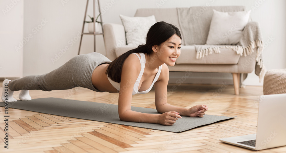 Fototapeta premium Online Training. Woman Exercising at Home, Doing Plank and Watching Videos on Laptop