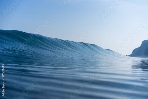 Obraz na plátně Water level view of a clean blue ocean wave forming smooth lines across the surface with soft light and open horizon