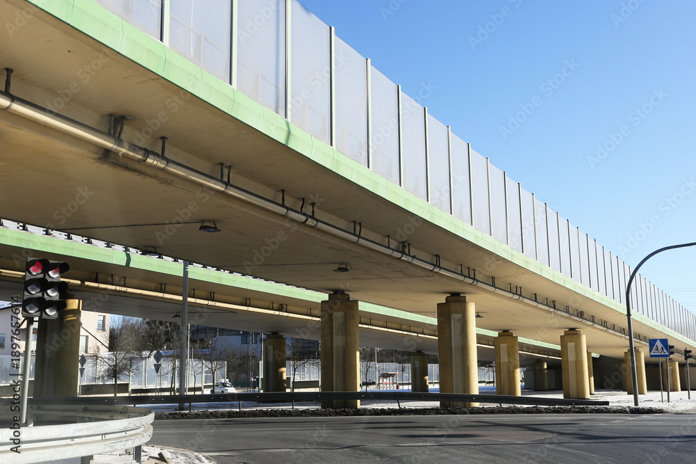 Obraz premium Urban road overpass structure. Concrete bridge with noise barriers. Empty city street below. Modern transport infrastructure scene. Winter light and clear sky. Architecture and traffic design.
