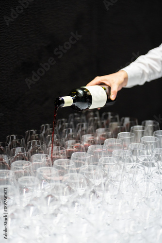 Hand pouring red wine into many glasses