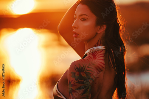 Young beautiful brunette woman romantic portrait at warm sunset light on sea shore, tattoo on body