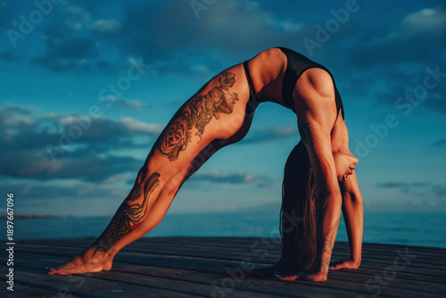 Young slim beautiful woman sports stretching on lake shore on summer day, tattoo on body