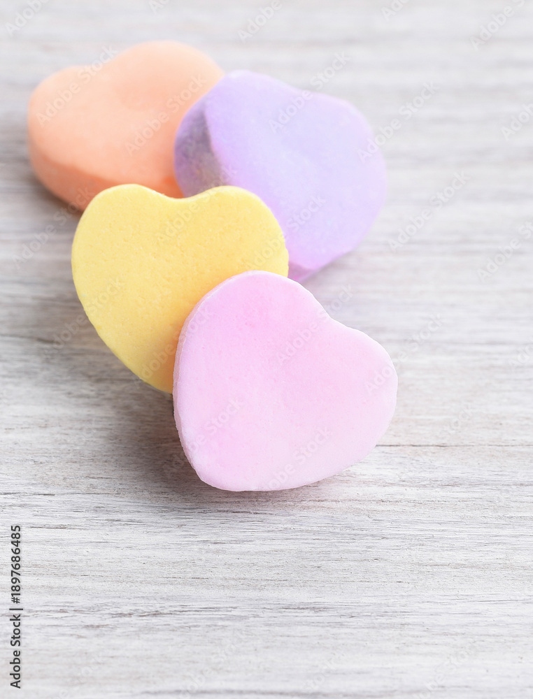Obraz premium Closeup with shallow depth of field of 4 pastel Valentine's Day heart shaped candies on a white wood surface.