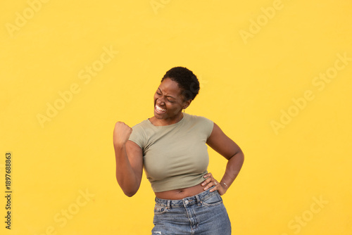Excited woman clenching fist to celebrate success against yellow background. Lady in casual clothes showing joyful expression and confident gesture