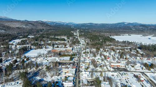 Downtown Schroon Lake, NY blanketed in snow during winter, showing roads, buildings, and forested surroundings from above.