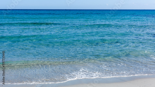 Fotografie Turquoise Mediterranean Sea waves gently lapping sandy shoreline of Sardinia