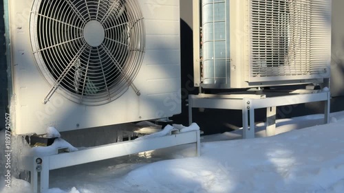 Heat Pump Outdoor Units Covered in Ice and Snow. Multiple heat pump units stand in deep snow with ice formation at their bases, illuminated by bright sun on a freezing winter day.