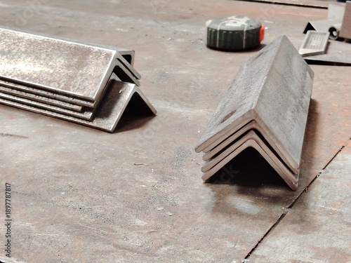 Industrial L-Shaped Steel Angle Bars Stacked on a Gritty Metal Workshop Workbench