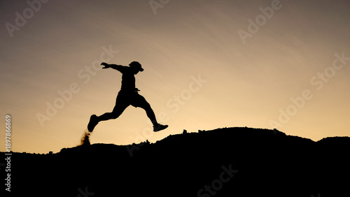 Wallpaper Mural A silhouetted individual leaps confidently across a small ridge against a backdrop of the setting sun, exuding energy and determination. Torontodigital.ca