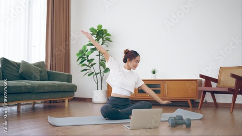 Happy young Asian woman practicing yoga and shoulder stretching at home sitting on floor in living room