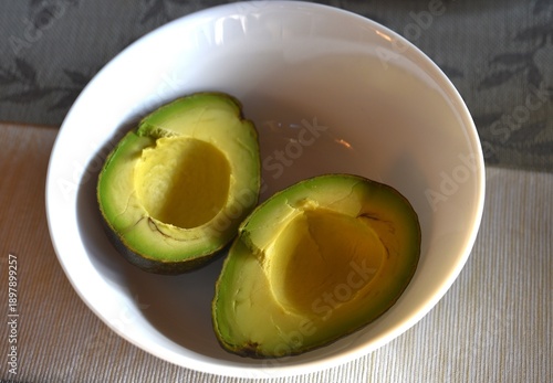 Avocado cut in half in white bowl.