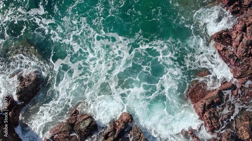 A cinematic slow motion drone orbit shot of white waves hitting dark rocky shoreline with crystal clear blue water in Flores, Indonesia.
